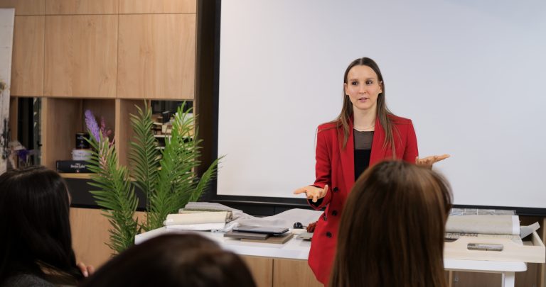 Woman in red blazer conducts business training session. Engaging audience with her expertise and confidence, effective business education and skill development in modern corporate environments.
